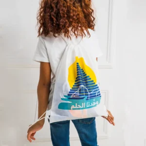طفل بشعر مجعد يظهر بظهره مرتديا حقيبة ظهر بيضاء عليها عبارة وحدنا الحلم